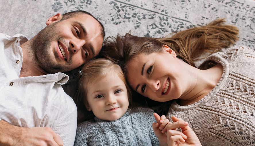 A family of 3 laying on the newly cleaned carpet.