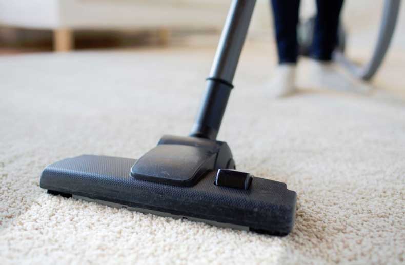 The image shows a man cleaning a carpet using a vacuum.