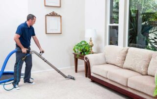The image shows a man cleaning a carpet using a vacuum.