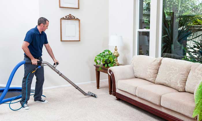 The image shows a man cleaning a carpet using a vacuum.