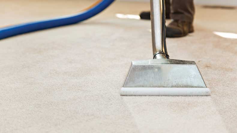 The image shows a man cleaning a carpet using a vacuum.