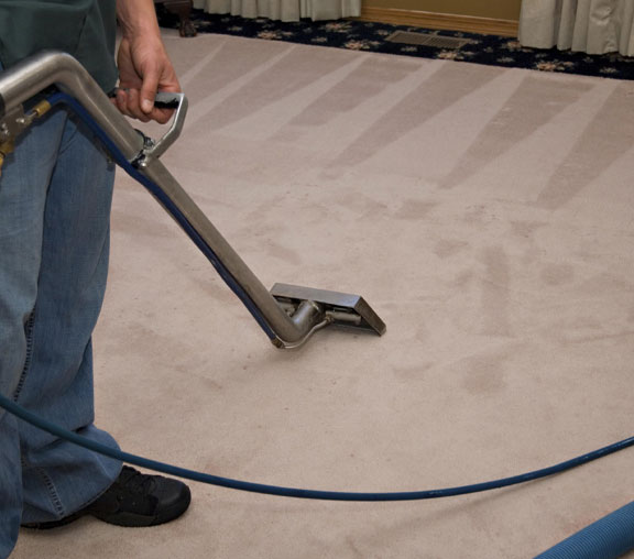 The image shows a man cleaning a carpet using a vacuum.