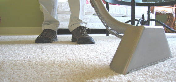 The image shows a man cleaning a carpet using a vacuum.